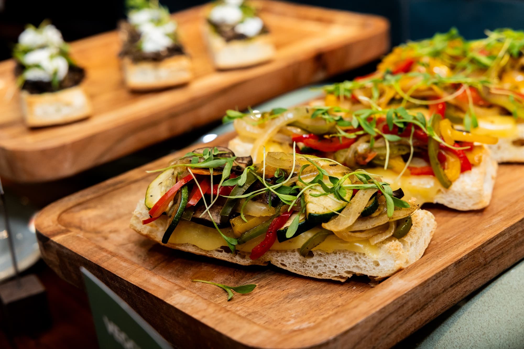 Toast bites with peppers and greens on wooden serving boards at a Cotidiano event